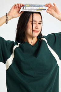 Person wearing a green and white outfit with books on their head against a plain background