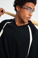 Person wearing glasses and a black outfit with white stripes, holding a wooden object.