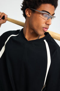 Person wearing glasses and a black outfit with white stripes, holding a wooden object.